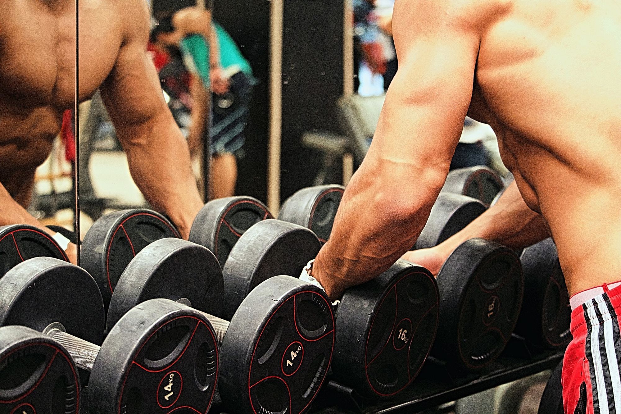 Topless athletic guy about to lift dumbbells off a weight rack