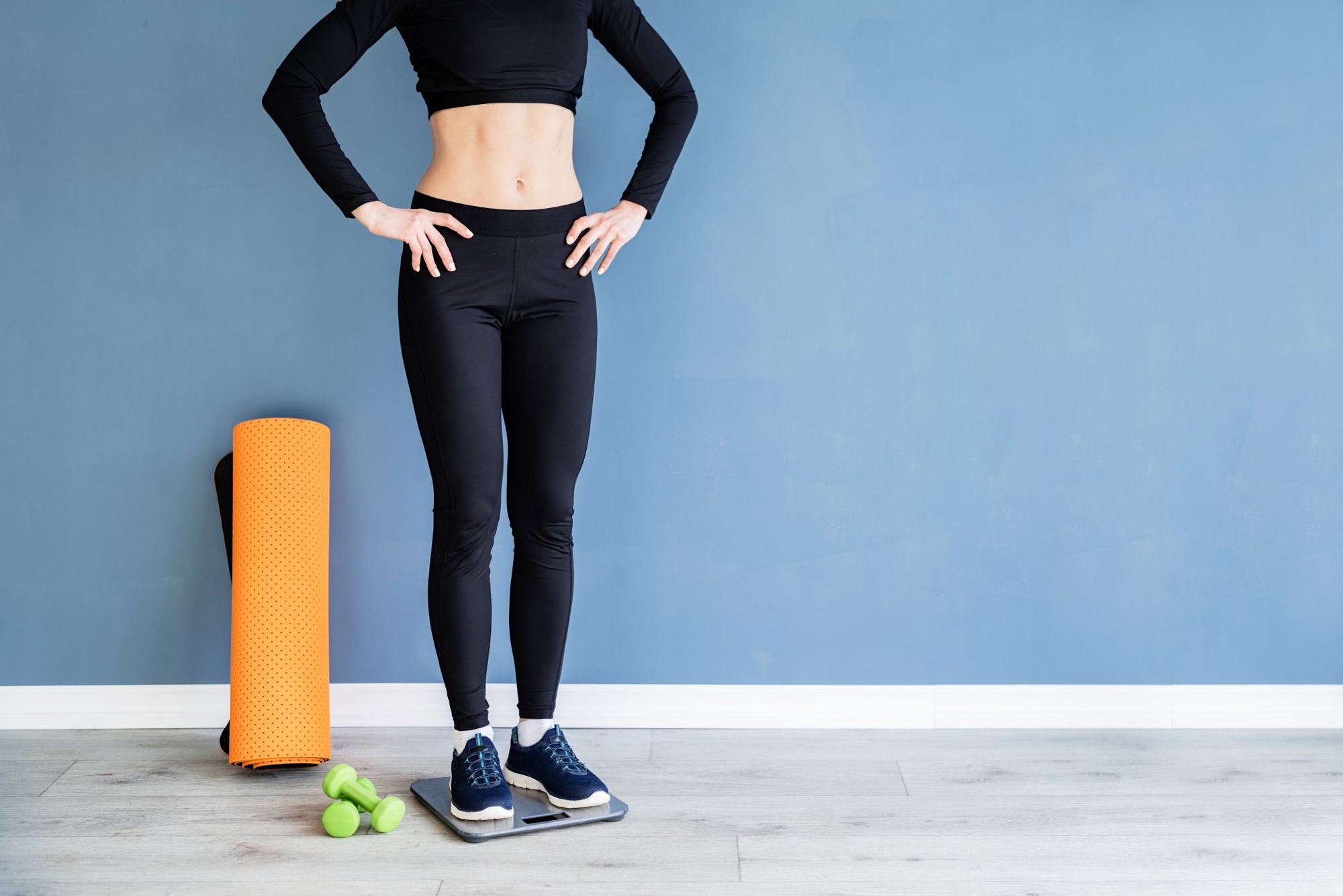 Young content woman in black sport clothes standing on scales