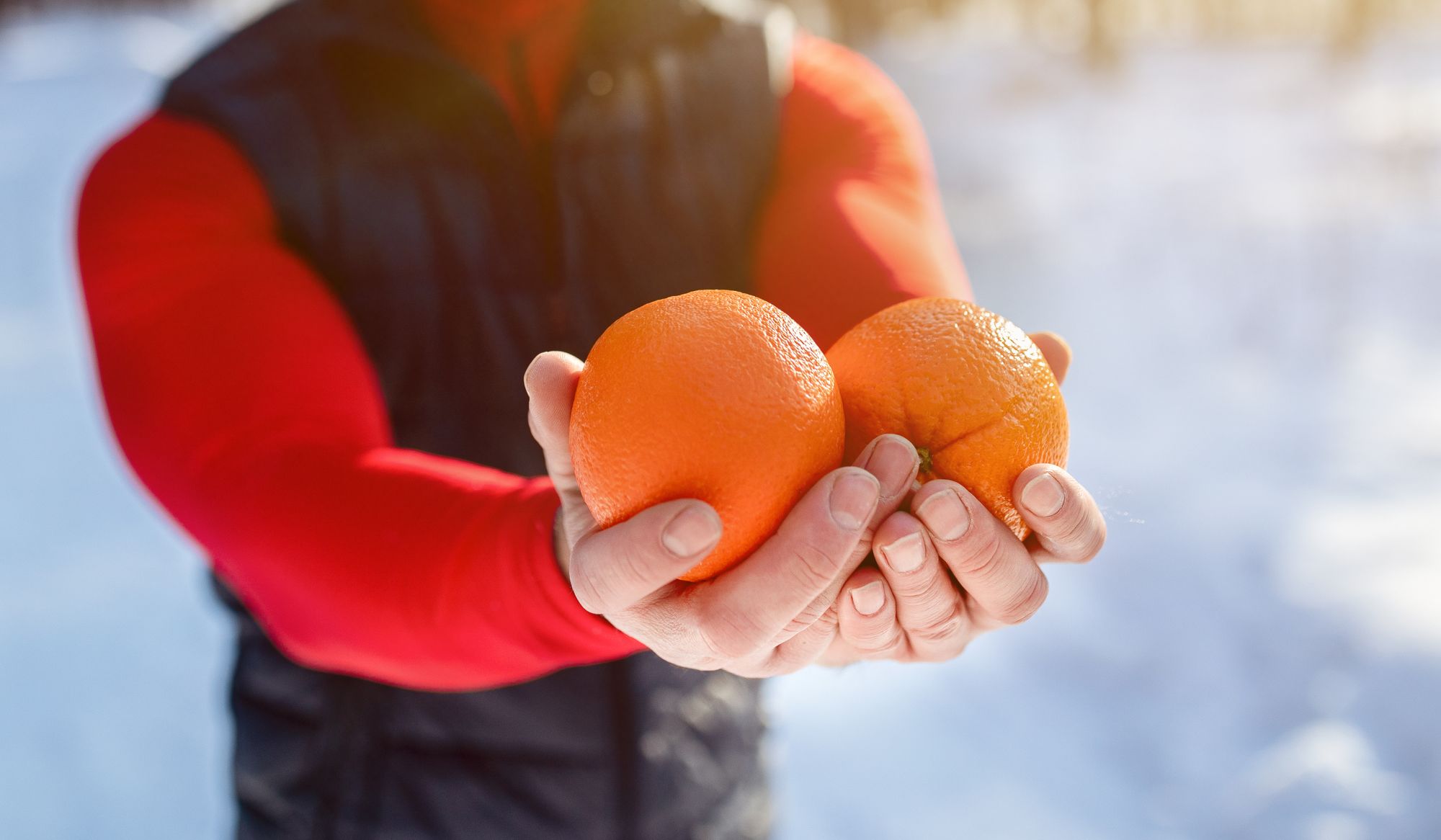 Closeup of fit mature man holding oranges as healthy snack after morning workout at snowy winter