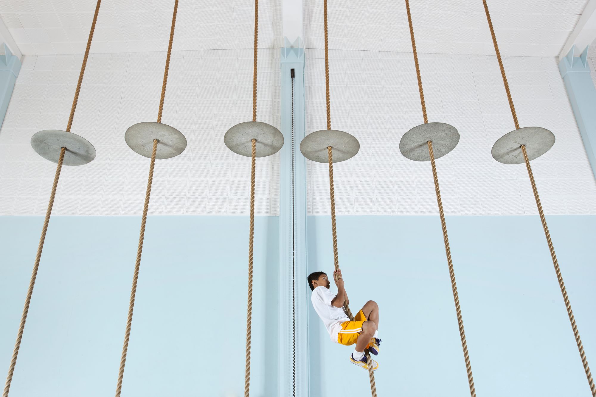 A boy climbing up a rope at the gym.