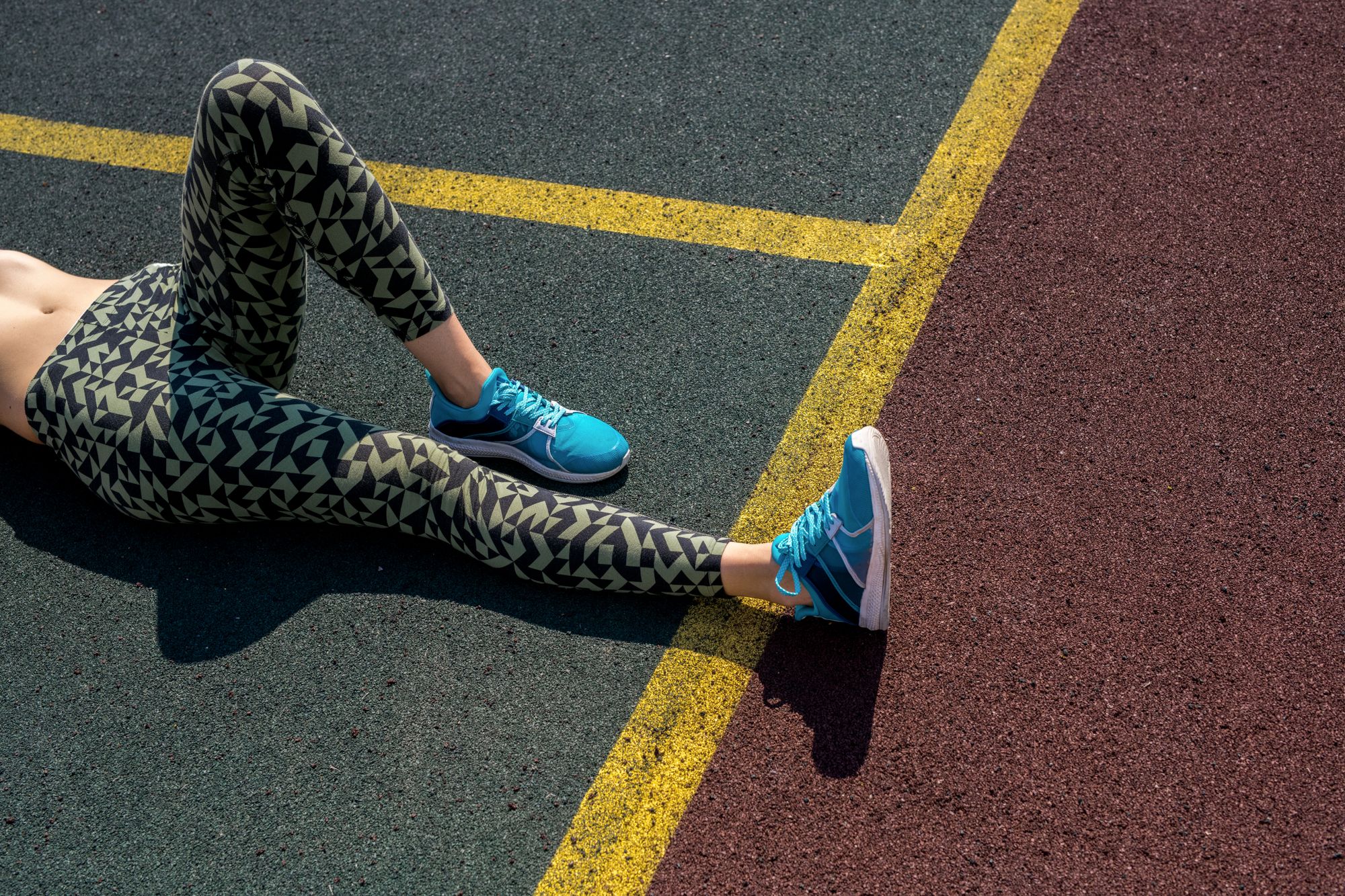 High angle portrait of unrecognizable young woman resting lying on ground in outdoor basketball court in sunlight, copy space