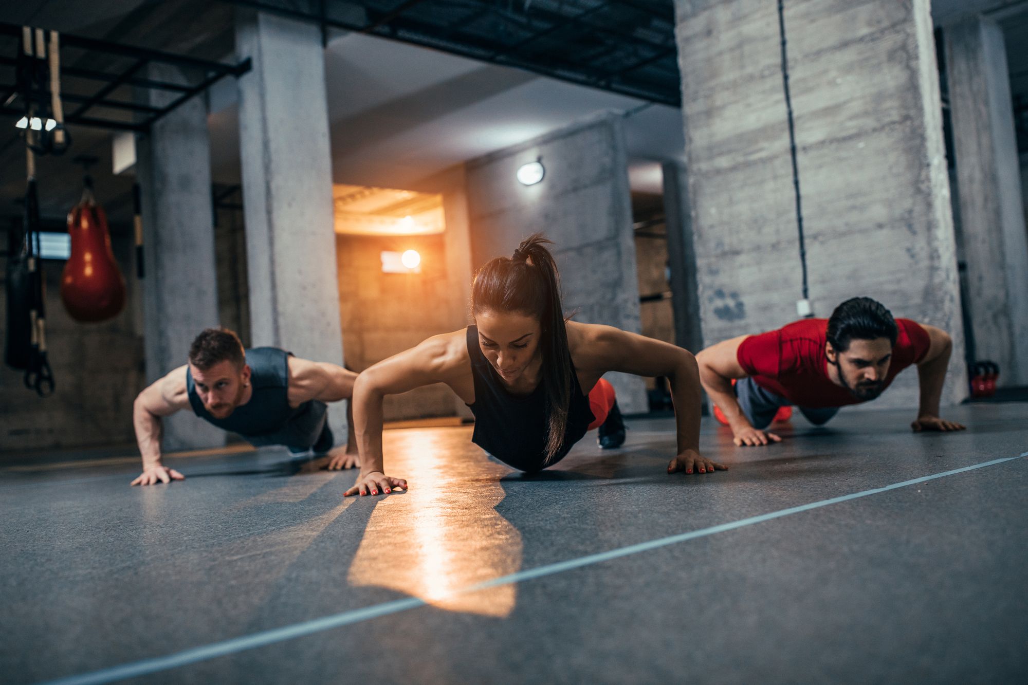 Shot of two young men and a woman standing in plank position at the gym