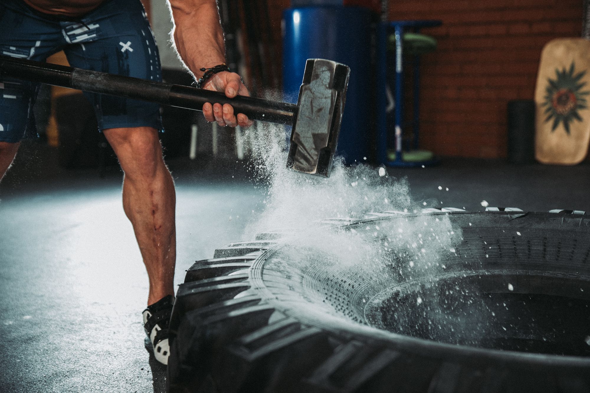 A photo of a man in a gym hitting a truck tire with a hammer