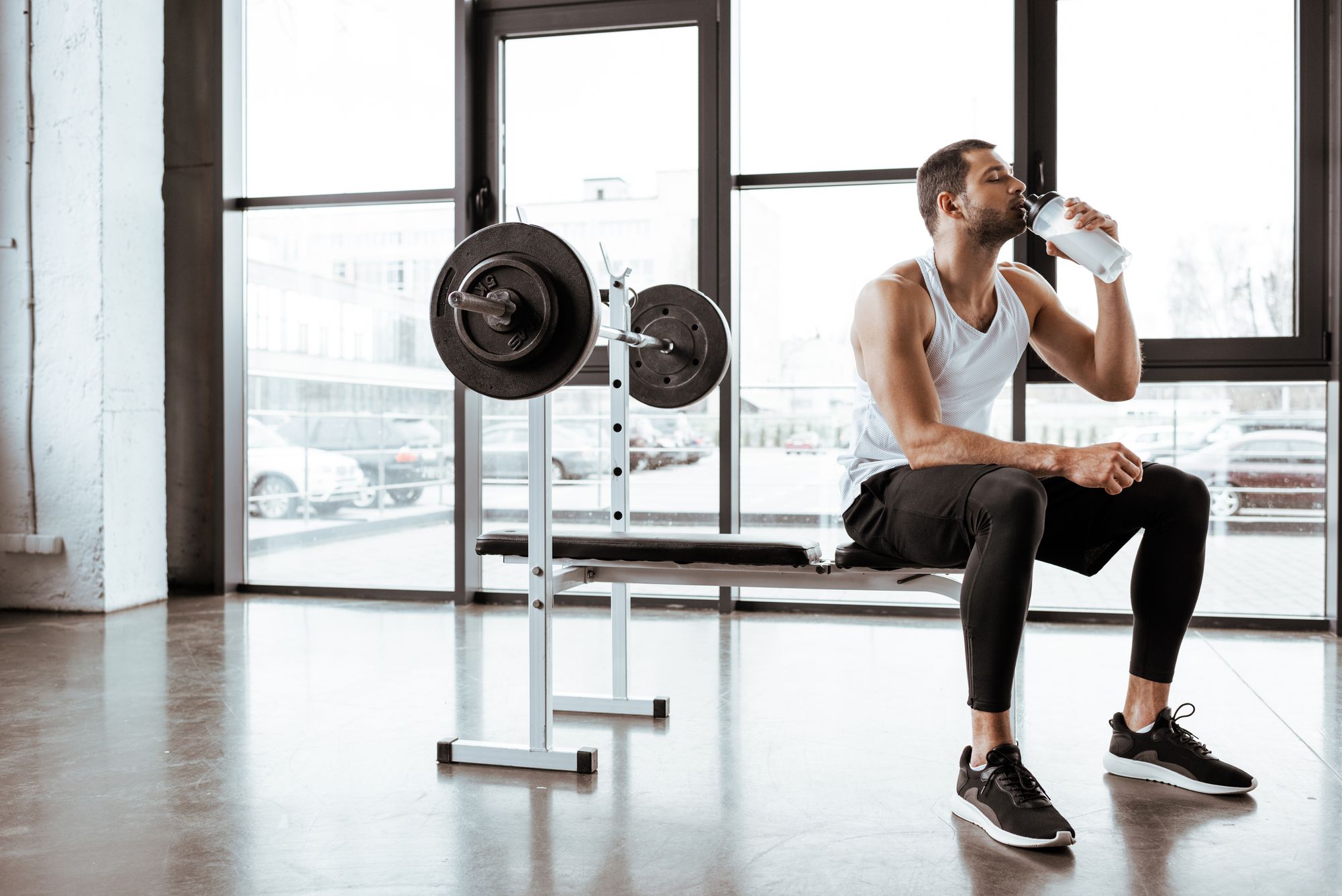 handsome sportsman drinking protein milkshake near barbell in gym