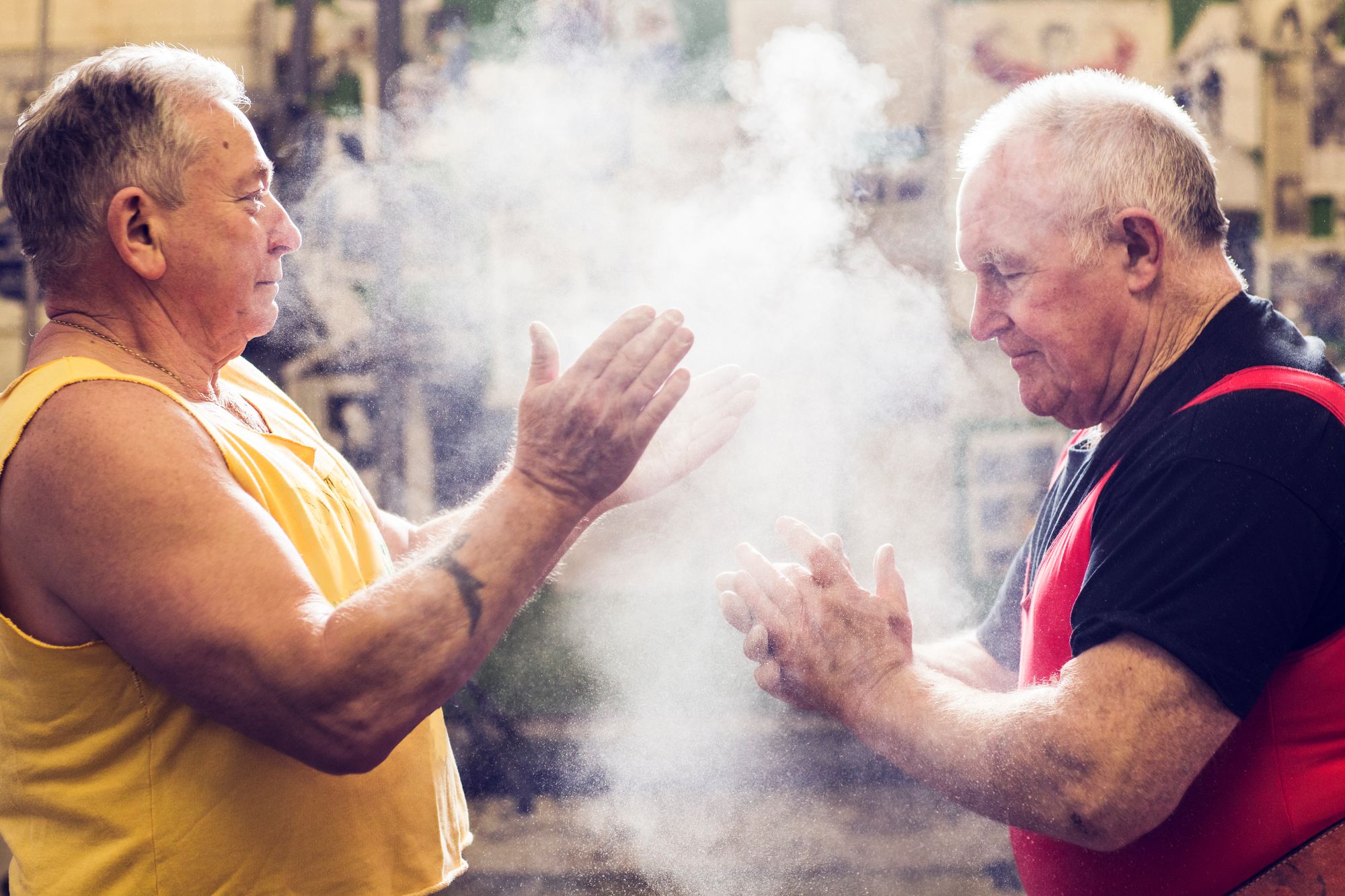 Two senior male powerlifters chalking their hands in gym