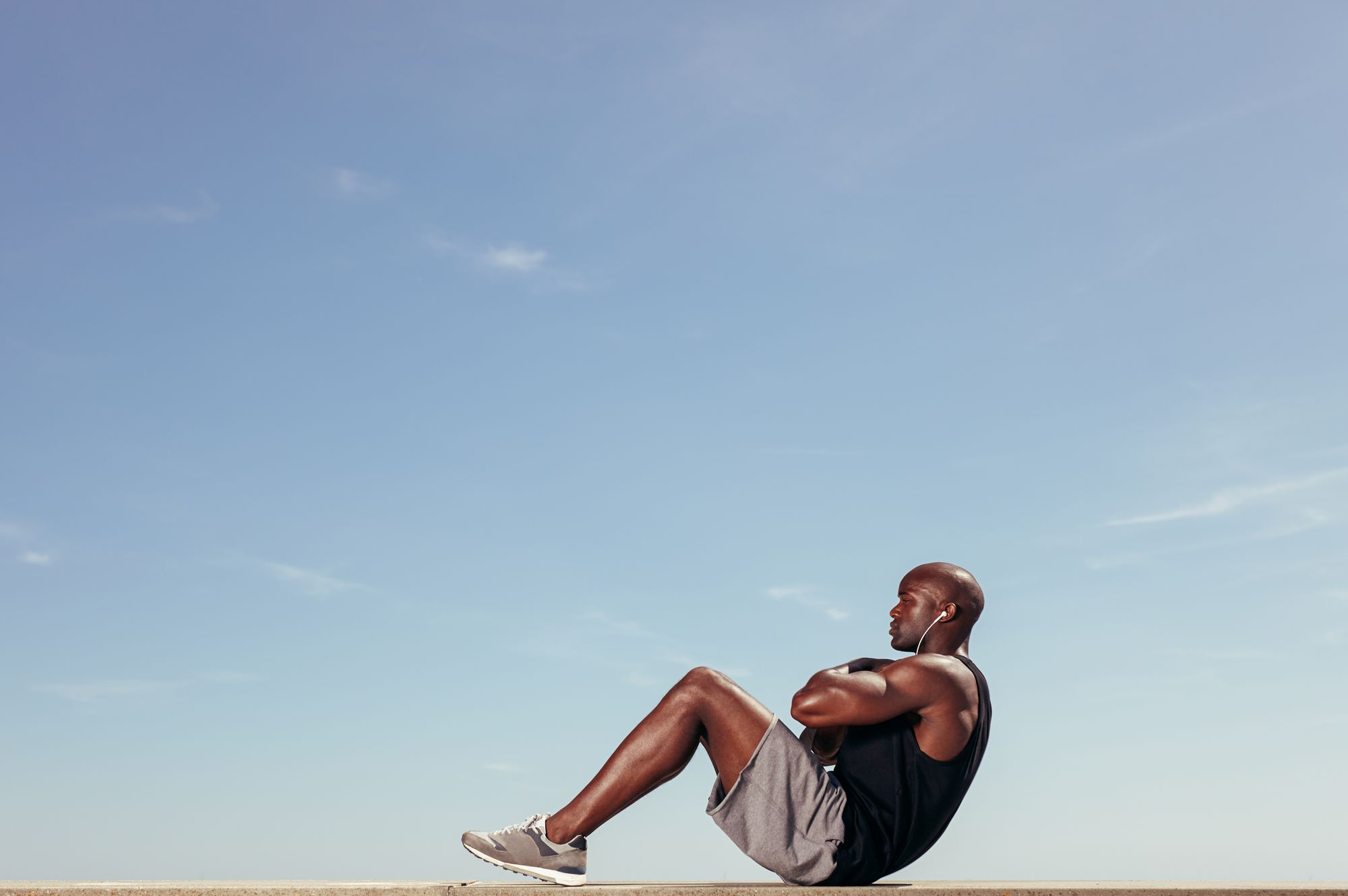 Young African man doing abdominal exercise outdoors.