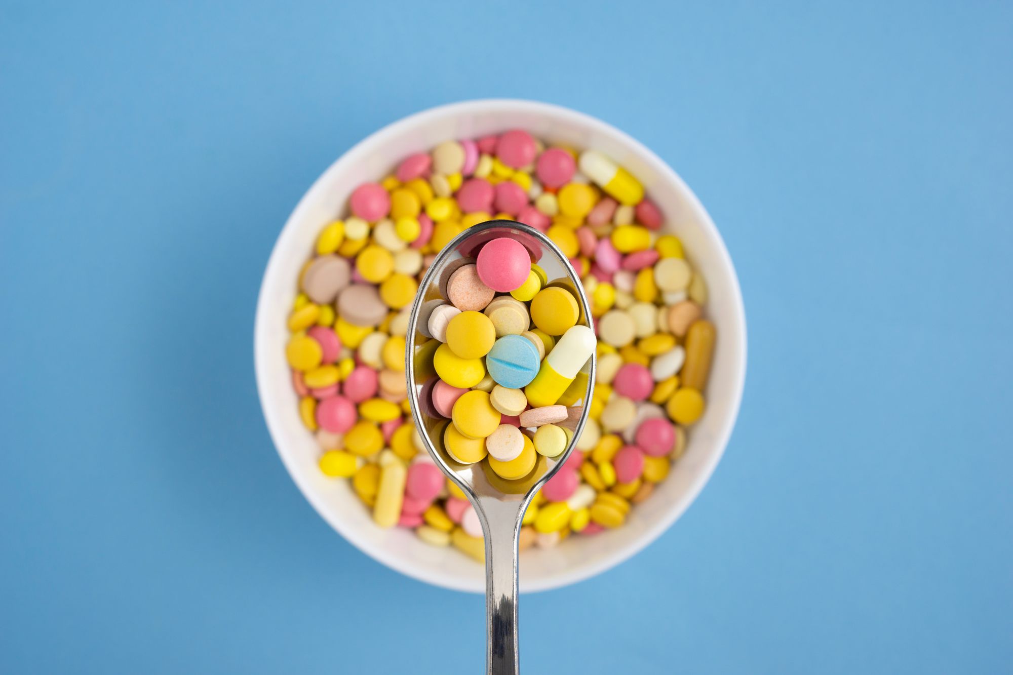 Creative health diet medicine concept photo of pills and drugs in plate with spoon on blue background.