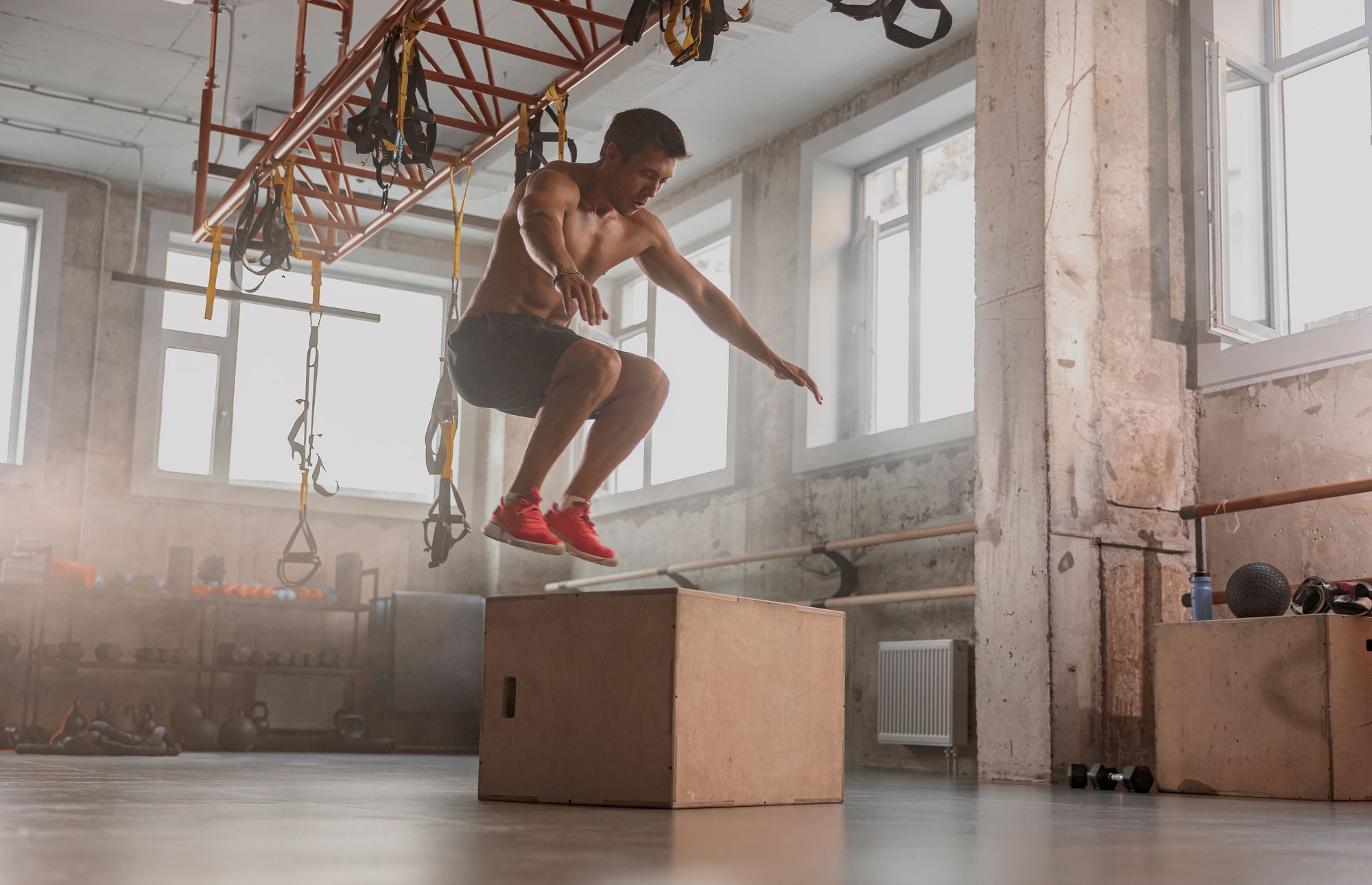 Side view of male athlete jumping on wooden box during sport training in fitness centre
