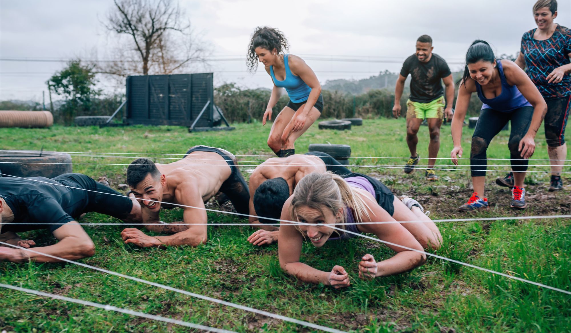 Group of participants in an obstacle course crawling under electrified cables