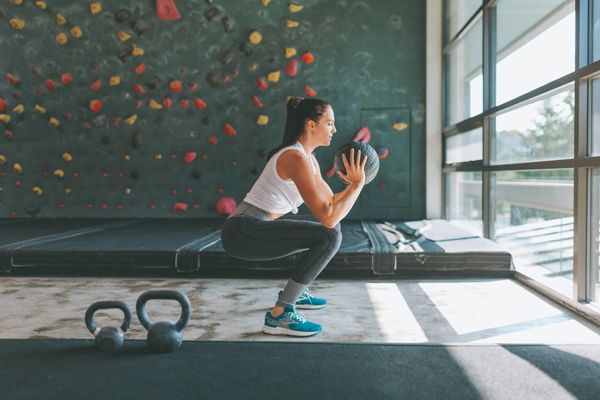 Woman doing medicine ball squats in front of a rock climbing wall