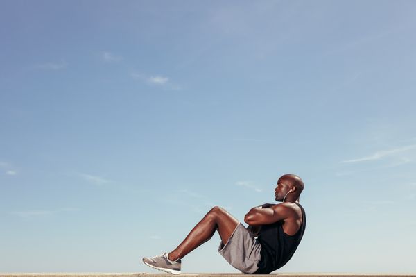 Young African man doing abdominal exercise outdoors.