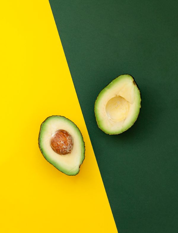 Organic avocado with seed, avocado halves and whole fruits on yellow and green background